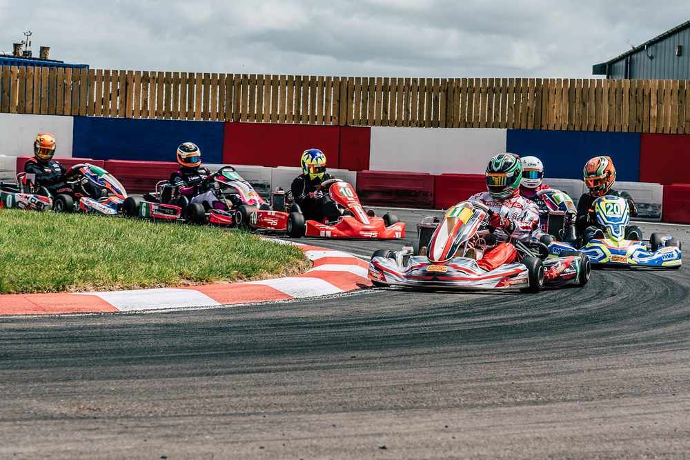 Plusieurs pilotes dans des karting colorés naviguent un virage de circuit
