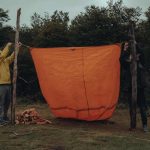 Trois personnes accrochent une grande toile orange entre deux poteaux