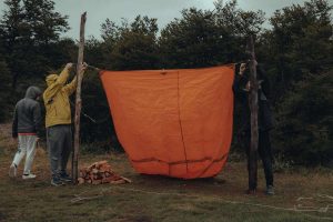 Trois personnes accrochent une grande toile orange entre deux poteaux