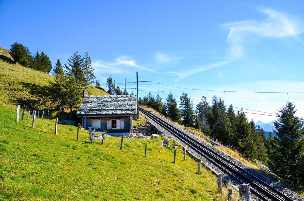Petit chalet en montagne avec funiculaire et sapins, paysage alpin verdoyant