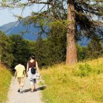 Deux randonneurs sur un sentier herbeux avec montagnes boisées en arrière-plan