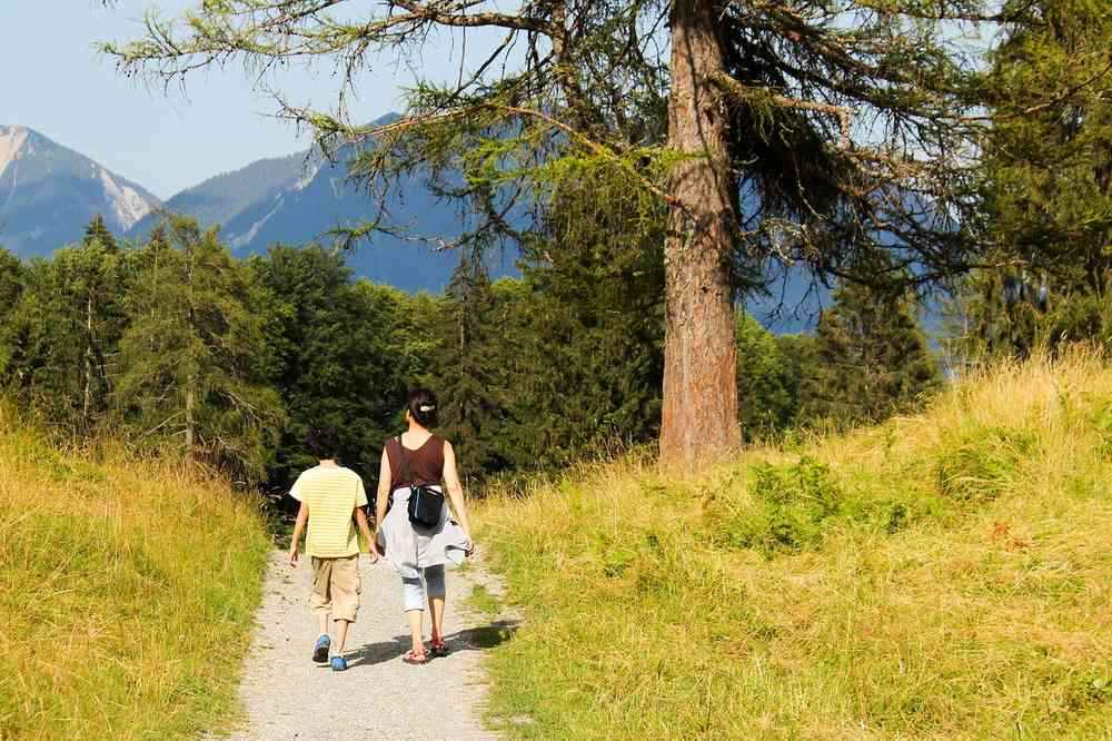 Deux randonneurs sur un sentier herbeux avec montagnes boisées en arrière-plan